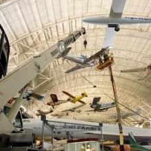 Museum staff members hang a silver monoplane onto the roof of the aircraft hangar at the Steven F. Udvar-Hazy Center.