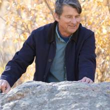 Karl G. Hufbauer, a man, stands outside behind a rock.