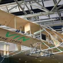 Biplane made with tan fabric and white metal hanging in the museum. "Vin Fiz" written on the bottom part of the lower wing in green paint.