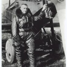 Lt. John Macready, a white man, stands in aviator gear next to an aircraft.