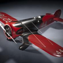 Model of a red and silver-colored monoplane with one engine. Number 44 is painted on the left wing and behind the cockpit of the plane.