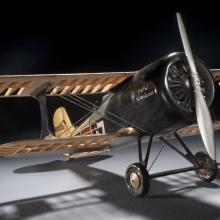 Front-facing view of wooden and black-colored metal biplane model with one engine.