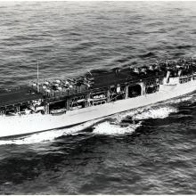 Side view of the first American aircraft carrier, a large boat that carried aircraft, in an ocean.