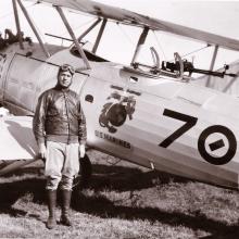 C. Frank Schilt, a white male pilot, stands next to an aircraft wearing aviator gear.