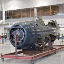 The fuselage of a blue military monoplane is the only aircraft inside the museum's restoration hangar.