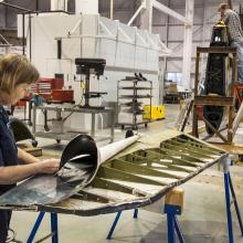 Two museum specialists perform conservation work on a blue military monoplane inside the Museum's restoration hangar.