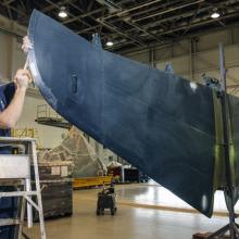 A male museum specialist prepares the tail section of a blue military monoplane for painting.