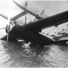 Charles Lindbergh stands atop an capsized aircraft, inspecting it for damage.