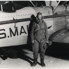 Charles Lindbergh stands in front of an aircraft wearing aviator gear.