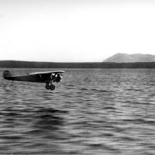 The Spirit of St. Louis, a monoplane with one engine flown by Charles Lindbergh, flies over a body of water.