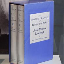 A blue bookcase featuring two books with silver-colored spines written by Anne Morrow Lindburgh about her flights with Charles Lindbergh.