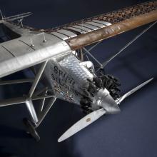 Top view of a cutaway model of the Spirit of St. Louis, a silver-colored monoplane with one engine. This view focuses on the nose and engine of the plane.