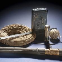 A set of emergency survival suplies including a fishing line and hook, a silver-colored blade, an emergency flare, a tan-colored roll of cord, an a metal container of emergency rations.