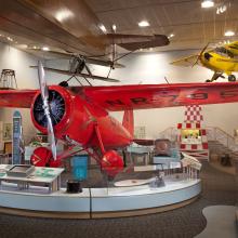 Front view of red monoplane with one engine. Registration number "NR7952" is painted on the lower side of the right wing.