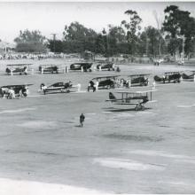 Two lines of early aircraft, mostly biplanes, are seen as part of an air race featuring only women pilots.