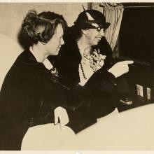 Amelia Earhart and Eleanor Roosevelt, both of whom are white women, sit and look at something not visible.