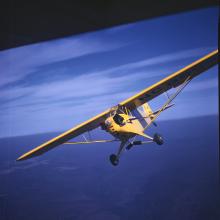 Front view of a yellow monoplane with one engine. The monoplane is in flight.