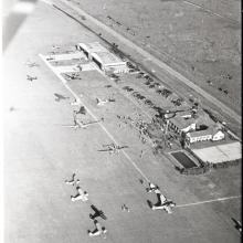 View of an aviation-focused country club from an aircraft. Planes are scattered near two buildings next to a road.