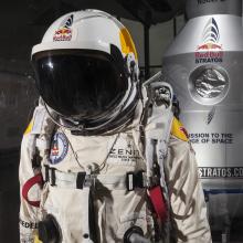 Close up of a high-altitude pressure suit used in a free-fall mission sponsored by Red Bull. The suit is a light-brown color and contains multiple tubes for life support. The helmet features a black sun visor.