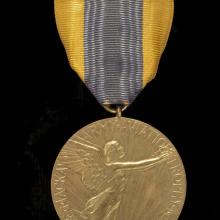 Front of aviation medal. Medallion features an etching of a person with wings in flight as well as the name of the trophy. Suspended using yellow and black fabric.