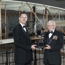 Two white men hold a trophy which was presented at the Museum.