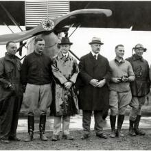 U.S. President Calvin Coolidge (a white man wearing a raincoat) stands with other white people at a meeting with pilots.