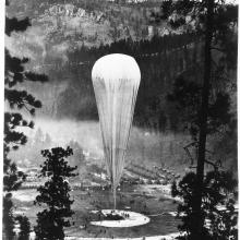 A tall air balloon sits on land in a forest clearing.