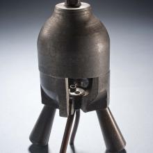 Metal rocket motor with four leg-like tubes below a cylinder-shaped combustion chamber. Small cutaway revealing the interior of the chamber.