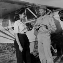 Two African American people stand in front of a small aircraft.