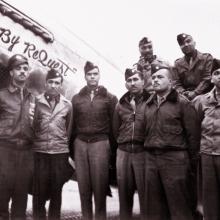 Benjamin O. Davis Jr., an African-American man standing third from the left, poses informally with members of his staff and other Tuskegee Airmen in front of a plane.