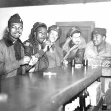 A group of Tuskegee Airmen sit and enjoy drinks and conversation at a bar.