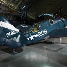 Dark blue and white military monoplane on display at the Museum. Monoplane has one engine. The number 208 is painte on the side and back fin of the plane.