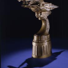 Side view of bronze-colored metal trophy with oblong topper shape.