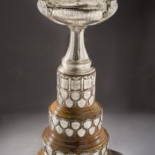 Aviation trophy with wooden tri-base holding military achievements on tiny plaques. The topper features four versions of Nike, Greek goddess of victory, holding a depiction of the Wright Military Flyer.