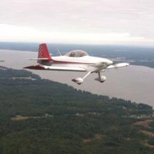 Side view of white and red monoplane with one engine and fixed landing gear. Monoplane is in flight.