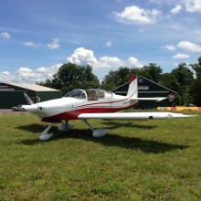 Side view of white and red monoplane with one engine and fixed landing gear.