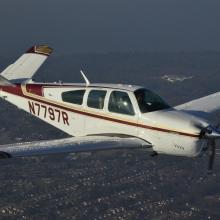 Side view of white and red monoplane in flight. Monoplane has one engine and registration number "N7797R" written in red on the back half of the fuselage.