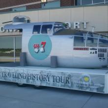 A plane's nose sits on a traveling exhibit trailer. The trailer has side detailing labelling it as part of a "traveling history tour".