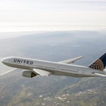 Side view of Boeing 777, a white commercial jet, in flight. The plane features white, blue, and yellow United Airlines livery.