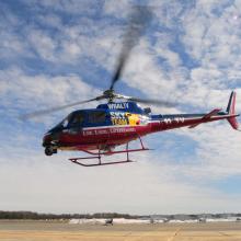 Side view of blue and red helicopter with three-blade top propellor. Helicopter is in flight.