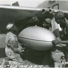 Members of a ground crew for a U.S. fighter group install a fuel tank onto the wing of a fighter plane.