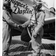 Clarence D. “Lucky” Lester and Andrew D. Turner, both of whom are African-American male pilots, shake each other's hand in front of an aircraft.