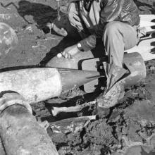 Lt. Elwood T. Driver, an African-American male pilot, sits and poses informally on top of rocket debris.