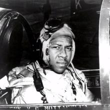 Jesse L. Brown, an African-American pilot who was part of the U.S. Navy, sits in the cockpit of an aircraft. He is wearing aviator gear.