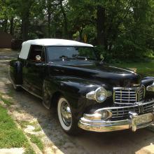 Diagonal front view of a black, two-door antique automobile with a white retractable roof.