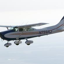 Side view of white monoplane in flight. Monoplane has one engine, fixed landing gear, and black and red accents. Registration number "N759AJ" is painted in black near the rear of the fuselage.