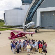 A group photo featuring several social media users who follow the Museum, the volunteers of an event, and the Museum's former director. They are standing on the runway in front of two aircraft.