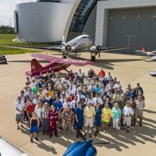 A group of pilots and crew members who participated in a pilot event at the Museum stand together with a former director of the Museum for a group photo.