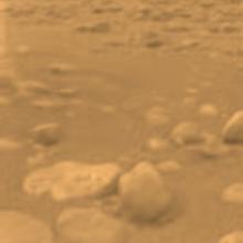 View of a part of the surface of Titan, a moon orbiting Saturn. The visible surface is rocky and is very uneven.