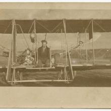 Harry Bingham Brown, a white male, sits at the cockpit of a Wright biplane.